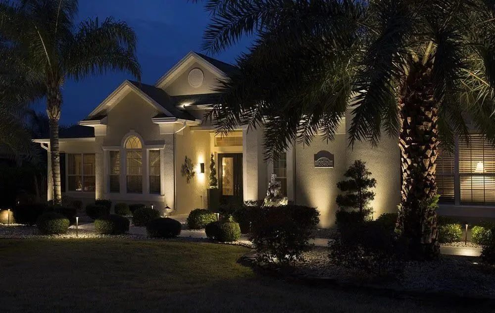 Front-yard landscape lighting at dusk, with lit palms, beds and entry