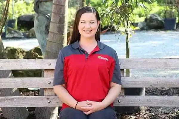 Brandi, Office Manager, smiling on a wooden bench outdoors in a red and gray polo shirt