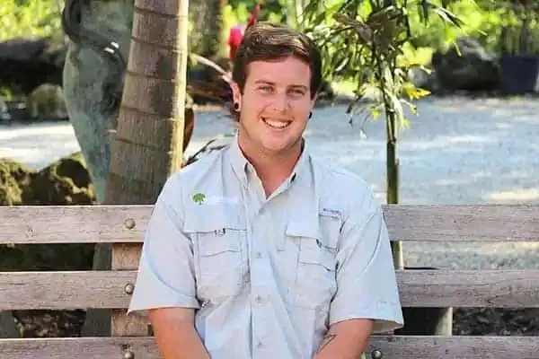 James “Jaime” Slayton Jr., Lead Designer, smiling on a wooden bench outdoors