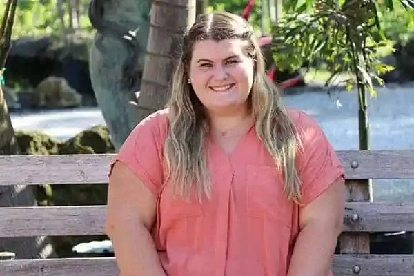 Madison Slayton, Social Media Director, smiling on a wooden bench in a garden setting